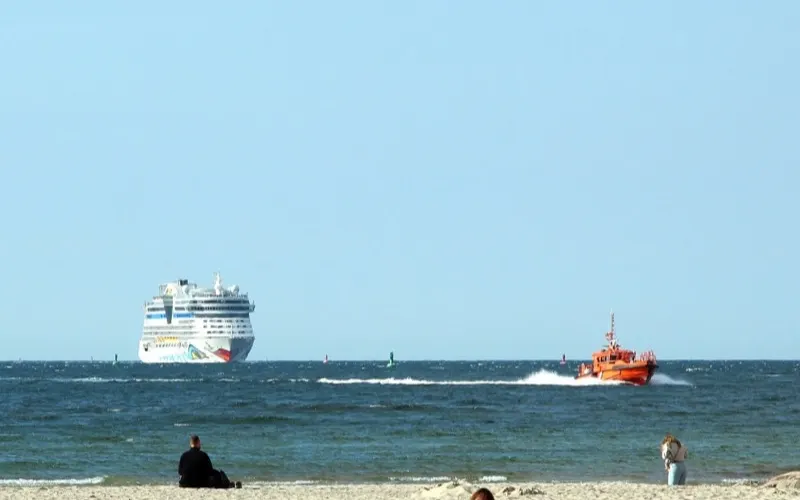 Kryssningsfartyg som lämnar inloppet till Warnemünde, sett från stranden
